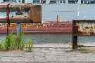 Leitplanke an der Kaimauer mit Containerschiff im Hintergrund